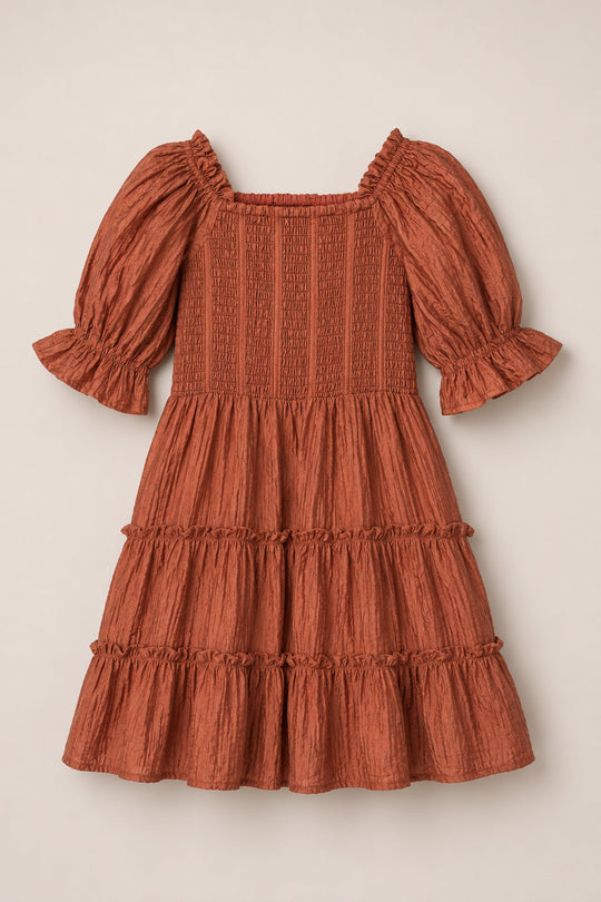 The Mini Madeline Dress in Apple Cider by Ivy City Co is a rust-colored, knee-length dress featuring puff sleeves, a square neckline, a smocked bodice, and a ruffled, tiered skirt. Crafted from textured, lightweight fabric, it’s perfect for casual or semi-formal occasions.