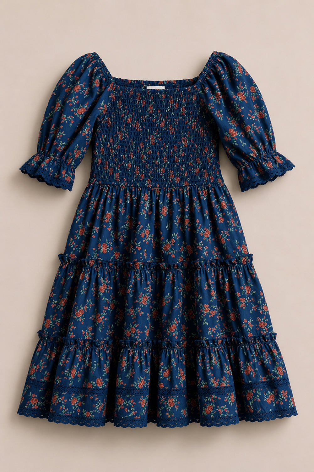The Mini Madeline Dress in Midnight Vibrant Chintz by Ivy City Co is a blue, knee-length dress featuring puffed short sleeves, a smocked bodice, and a tiered skirt. This charming floral chintz piece showcases a delicate red and orange print on a dark blue background.