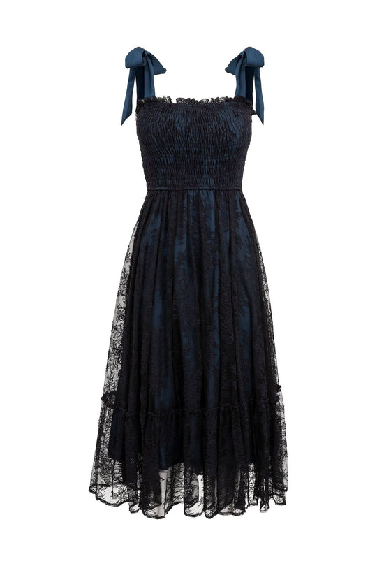 The Isadora Dress in Navy & Black by Ivy City Co features a knee-length silhouette with a lace overlay, shirred bodice, ruffled hem, and ribbon tie shoulder straps. Displayed on a white background, this stylish piece is designed to be maternity friendly.