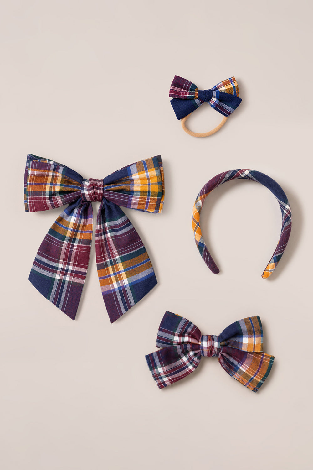 Four plaid accessories from Ivy City Co arranged on a beige background: two Hair Bows in Midnight Plaid, one matching headband, and one hair tie—all featuring Ivy City Co’s signature Midnight Plaid pattern in purple, yellow, blue, and white.
