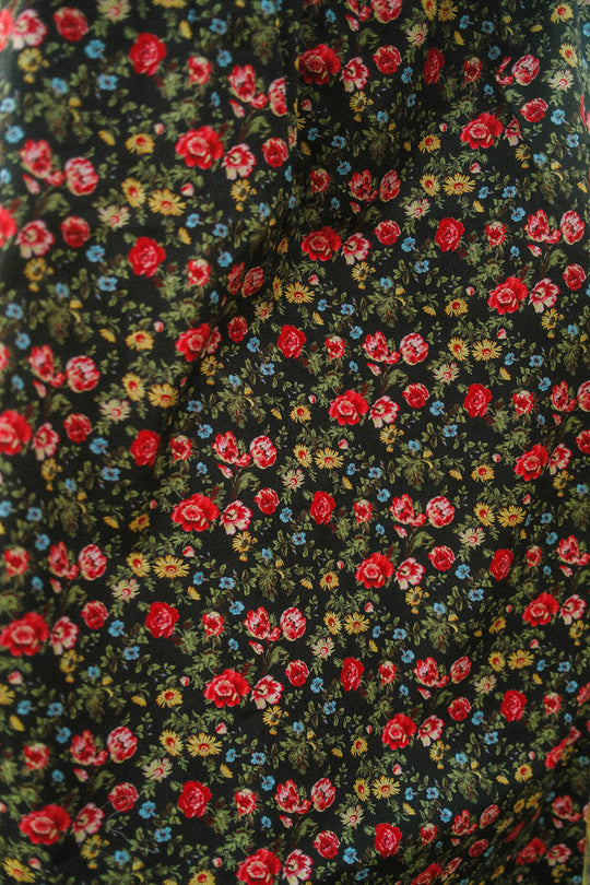 Close-up of black fabric adorned with a dense floral pattern featuring red roses, blue and yellow flowers, and green leaves. The material is softly gathered or draped, highlighting the intricate details of the Ivy City Co Annalise Dress in Obsidian Vintage Poppies—a stylish choice designed to be maternity friendly.