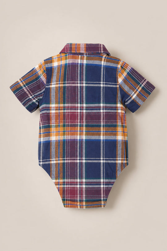 The Ivy City Co Baby Boy James Romper in Midnight Plaid is a short-sleeve collared bodysuit, showcased flat with the back facing up and featuring a multicolored plaid pattern in navy, yellow, red, and white.