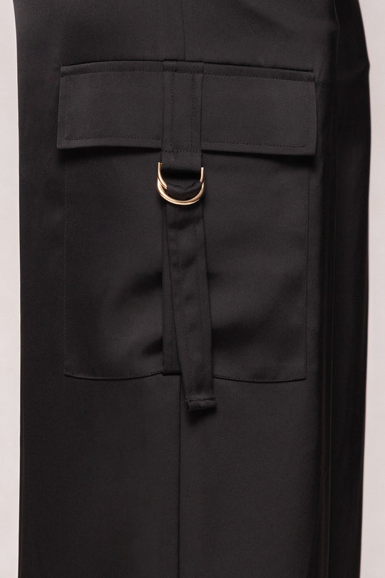 Close-up of a black pocket with a flap and a fabric strap featuring two gold D-rings, showcasing the modern loose fit of the Ivy City Co Shay Satin Pants in Black.