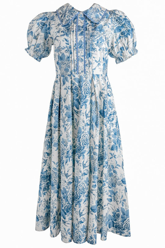 The Sophia Dress in Blue Floral by Ivy City Co is a vintage-inspired, ankle-length dress showcasing a charming blue floral pattern on a white background. Designed with puffed short sleeves, a wide collar, and pleated bodice details, this nursing-friendly dress offers both comfort and timeless style.