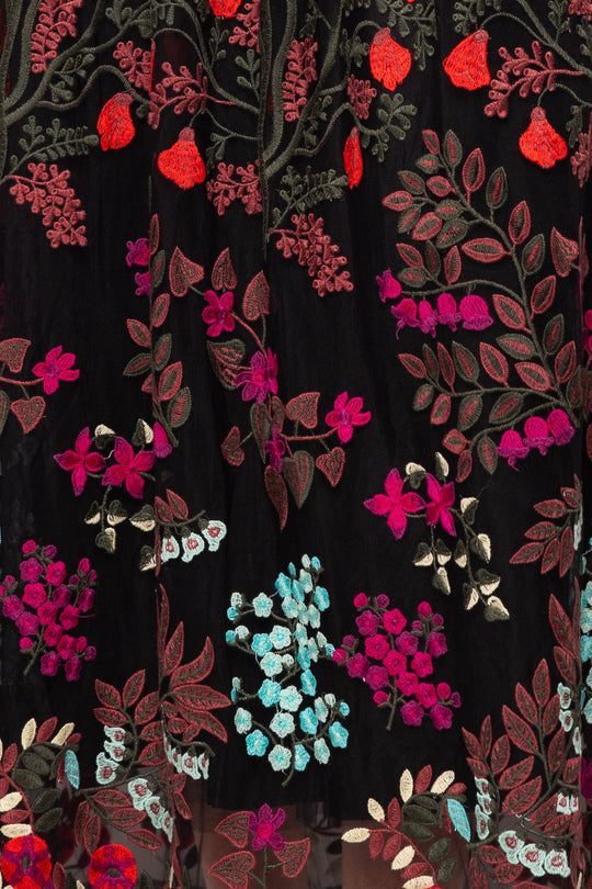 Moonlit Blossom black fabric from Ivy City Co’s Flora Dress features colorful floral embroidery in red, pink, blue, and green threads that create intricate leaves and clusters of flowers in a decorative, dense pattern—perfect for an elegant embroidered floral look or a statement Flora Dress.