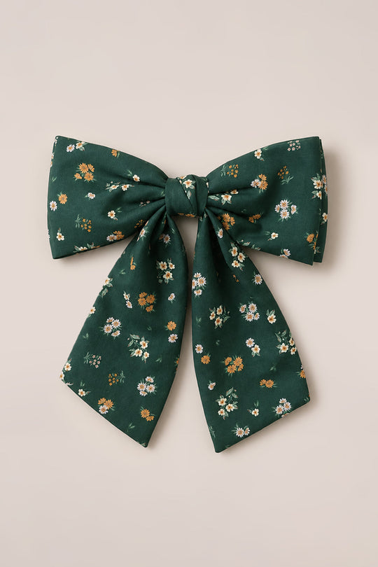 The Ivy City Co Hair Bow in Evergreen Lovelorn Ditsy features a large, green cotton design adorned with a floral print of small yellow, white, and orange flowers, beautifully displayed on a neutral background.