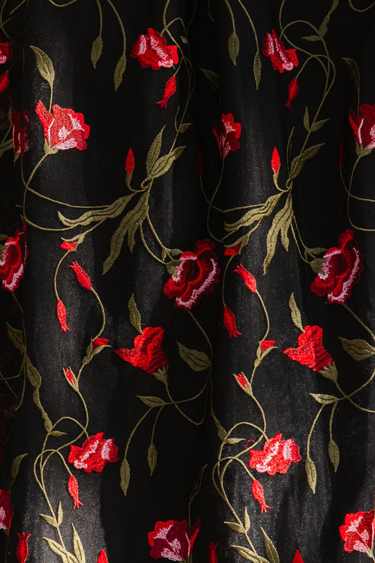 Black fabric with an embroidered floral pattern featuring red roses and green leaves is beautifully scattered across the mesh overlay, creating a decorative and elegant design reminiscent of the Flora Dress in Romantic Roses by Ivy City Co.