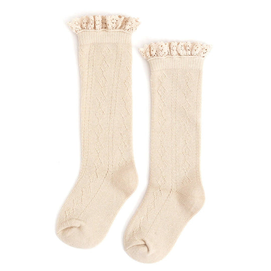 The Fancy Lace-Top Knee-High Socks in Vanilla by Little Stocking Co. feature a subtle zigzag pattern and delicate ruffled lace trim, perfect for girls who love classic style.