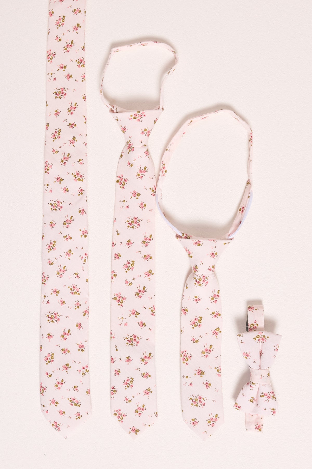 Four matching accessories from Ivy City Co—Ties in Madeline Pink Floral, including two neckties and a boys bow tie—are arranged on a light surface.