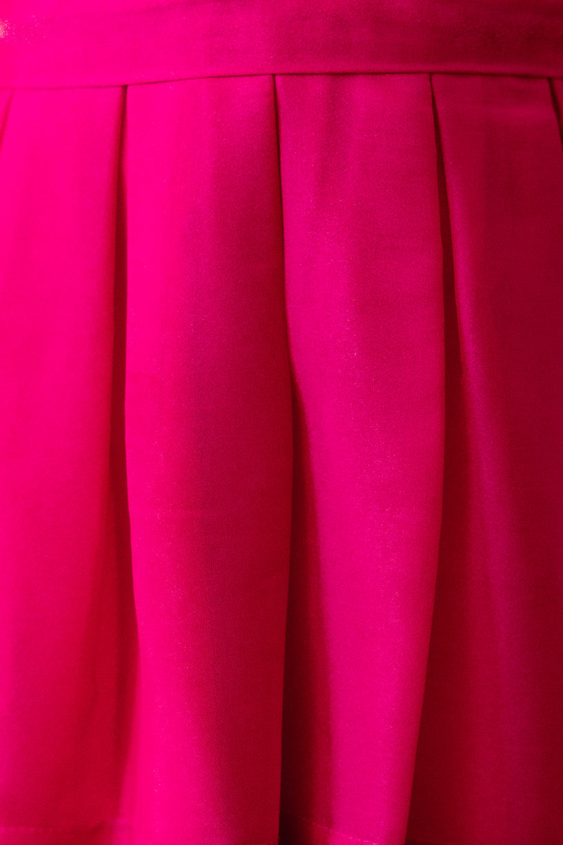Close-up of the Mini Cassian Dress in Hot Pink by Ivy City Co, highlighting the vivid pink pleated fabric and vertical fold lines that showcase its detailed texture.