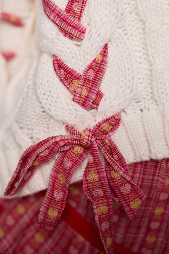 Close-up of the Agatha Sweater in Ivory by Ivy City Co—a women’s spring sweater in a white knit with braided details, adorned with pink patterned fabric ribbons and yellow dots. A matching pink fabric peeks out underneath, accentuating the open layered silhouette that’s perfect for the season.