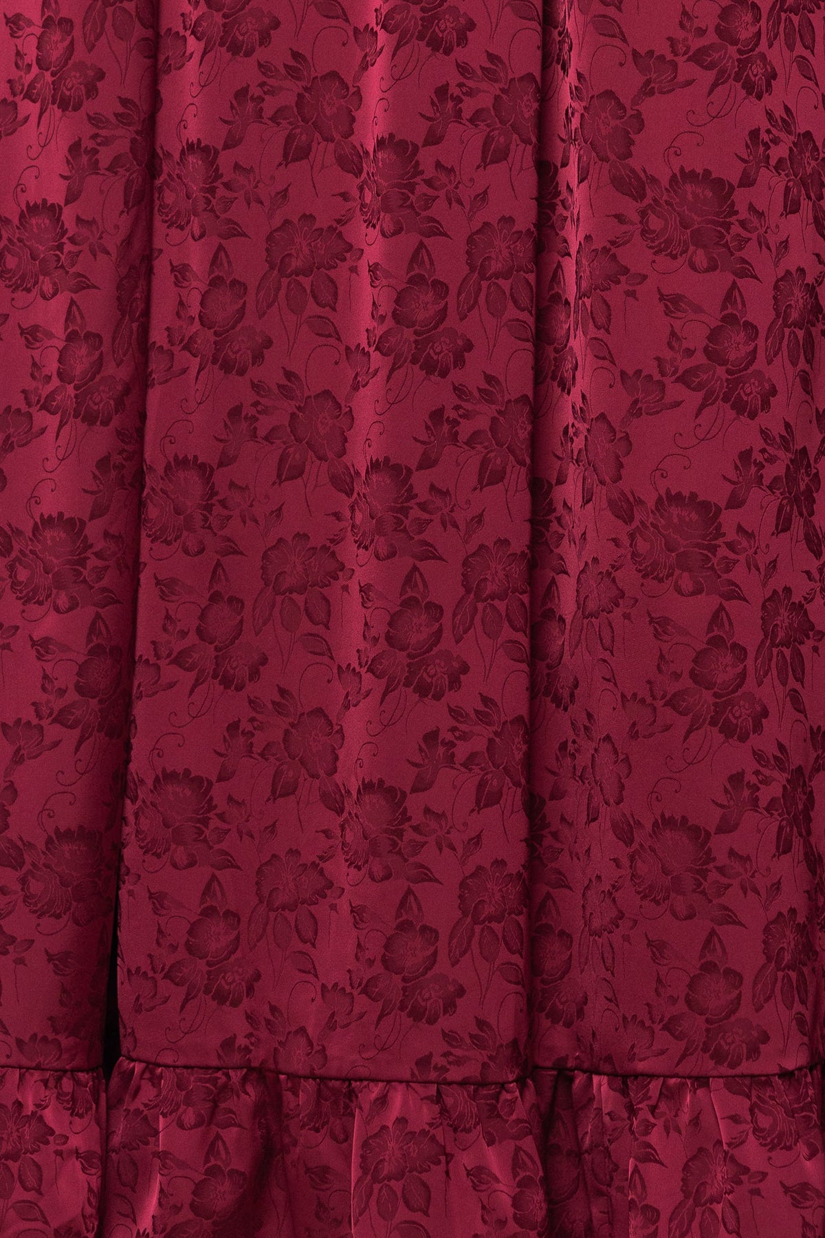 Close-up of deep red fabric with a subtle floral jacquard pattern and gathered ruffle detail at the hem, highlighting the elegant texture of the Amira Dress in Red by Ivy City Co.