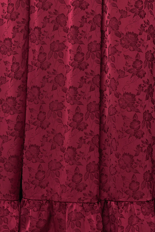 Close-up of deep red fabric with a subtle floral jacquard pattern and gathered ruffle detail at the hem, highlighting the elegant texture of the Amira Dress in Red by Ivy City Co.