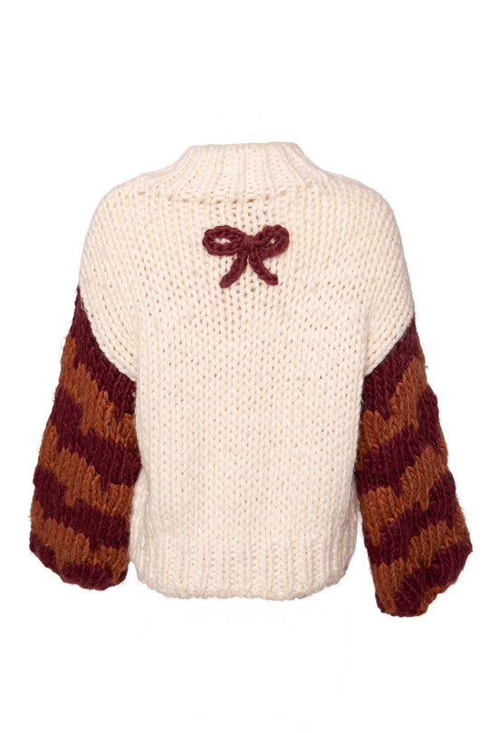 The Aimee Sweater in Orange & Cream by Ivy City Co is a chunky wool blend with a cream body, oversized sleeves with maroon and brown stripes, and a small maroon bow at the upper back.