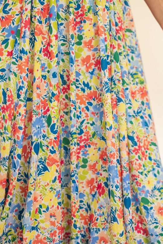A close-up of the Ada Dress in Vibrant Yarrow Print by Ivy City Co, featuring a flowing floral chiffon design in lively shades of blue, red, yellow, green, and orange. The lightweight fabric gives this piece a summery and graceful look—an ideal maternity-friendly choice that blends comfort with vibrant style.