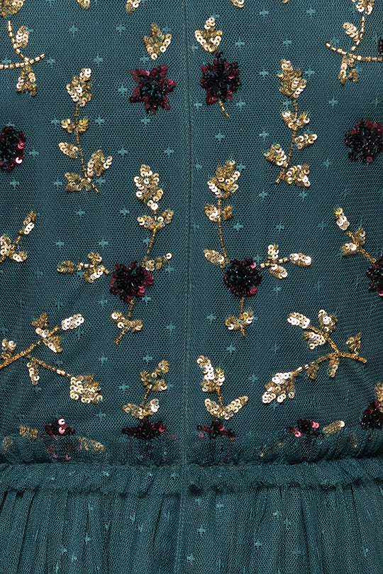 Close-up of the Adara Dress in Green by Ivy City Co: dark green fabric adorned with gold sequin floral embroidery and small burgundy sequin flowers, featuring intricate patterns and gathered tulle at the hem for a truly exquisite embroidered gown.