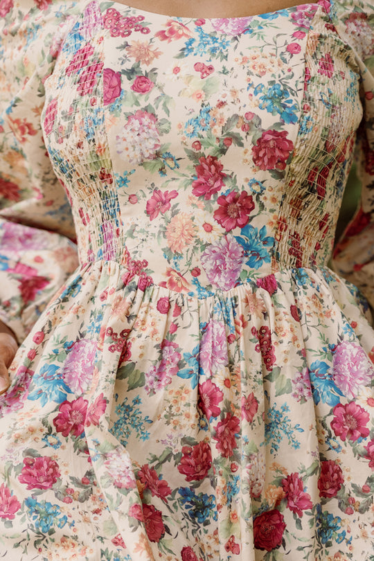 A close-up of a person wearing the Adelpha Dress in Autumn Amity Floral by Ivy City Co, a vibrant cotton maternity and nursing-friendly design showcasing colorful pink, red, blue, and green florals on a light background.