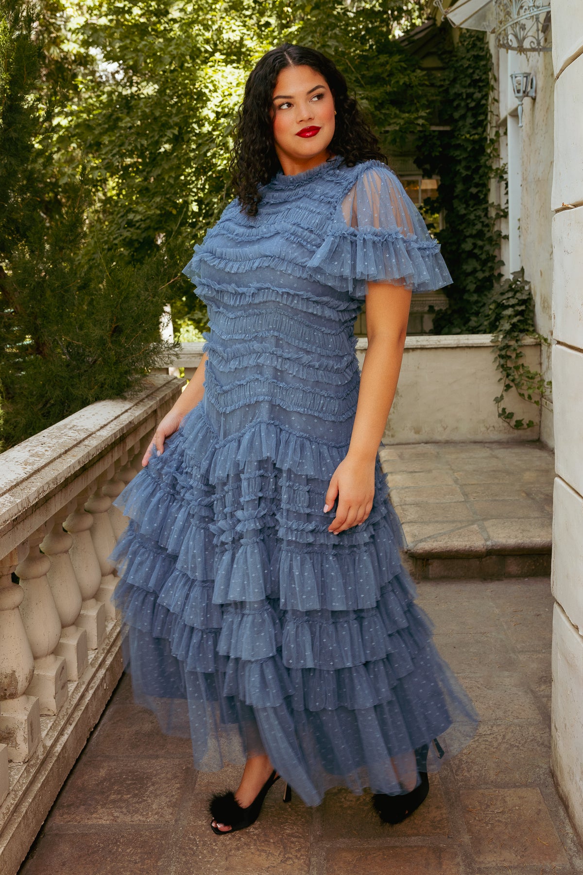 Woman wearing a blue tiered dress standing on a stone path with greenery in the background