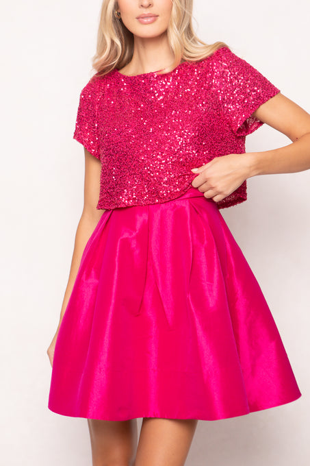 Woman wearing a bright pink sequin top and skirt set against a white background