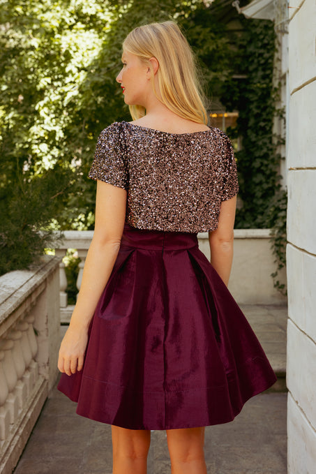 Young girl wearing a sequined top and burgundy skirt on a balcony.