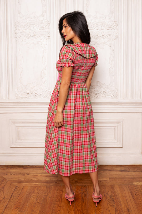 Woman wearing a red plaid dress standing against a white wall.