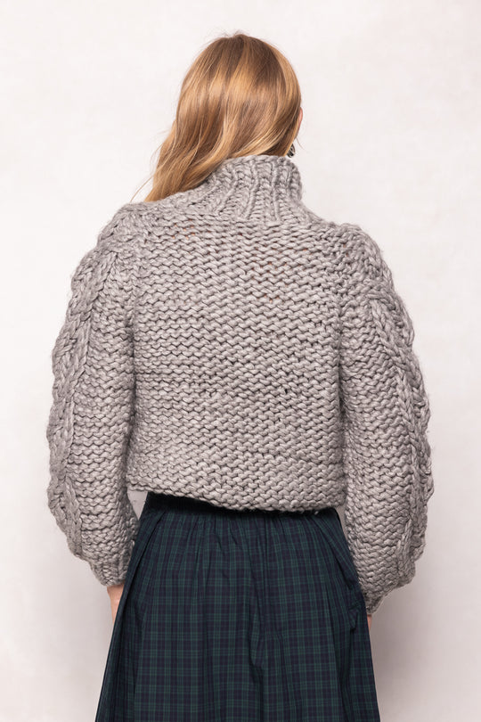 Person wearing a chunky knit gray sweater on a white background