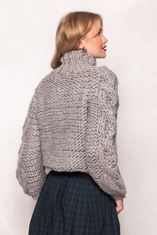 Woman wearing a chunky knit sweater against a plain background