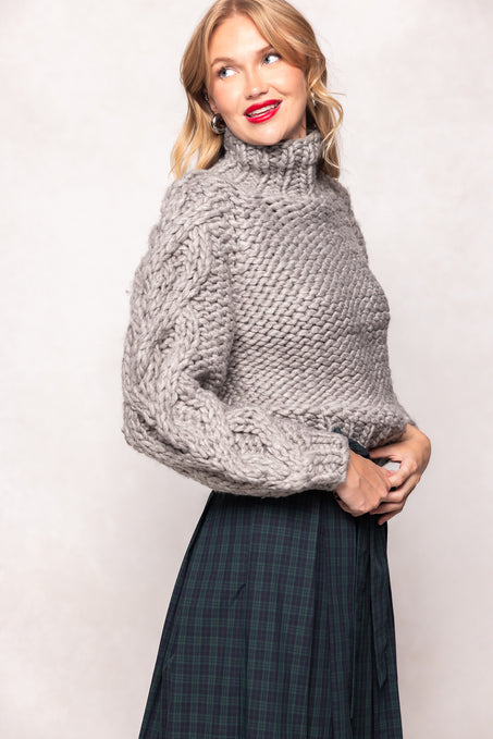 Woman wearing a chunky knit sweater and plaid skirt against a plain background