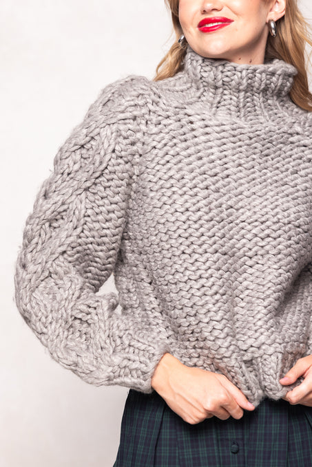 Person wearing a chunky knit gray sweater against a plain background