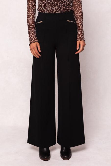 Person wearing black wide-leg pants with a leopard print top on a white background