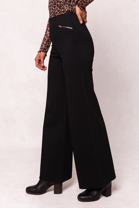 Person wearing black wide-leg pants with a leopard print top on a white background