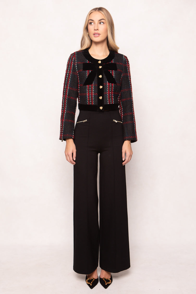 Woman wearing a patterned jacket with a bow and black pants on a white background