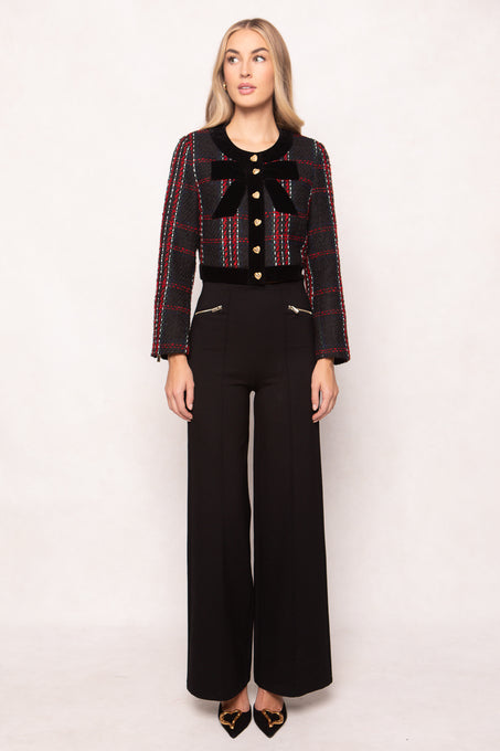 Woman wearing a patterned jacket with a bow and black pants on a white background