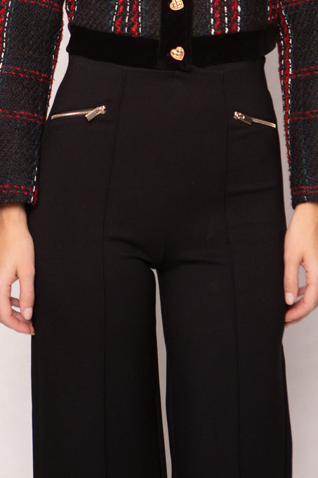 Black pants with gold zippers worn by a person, against a neutral background