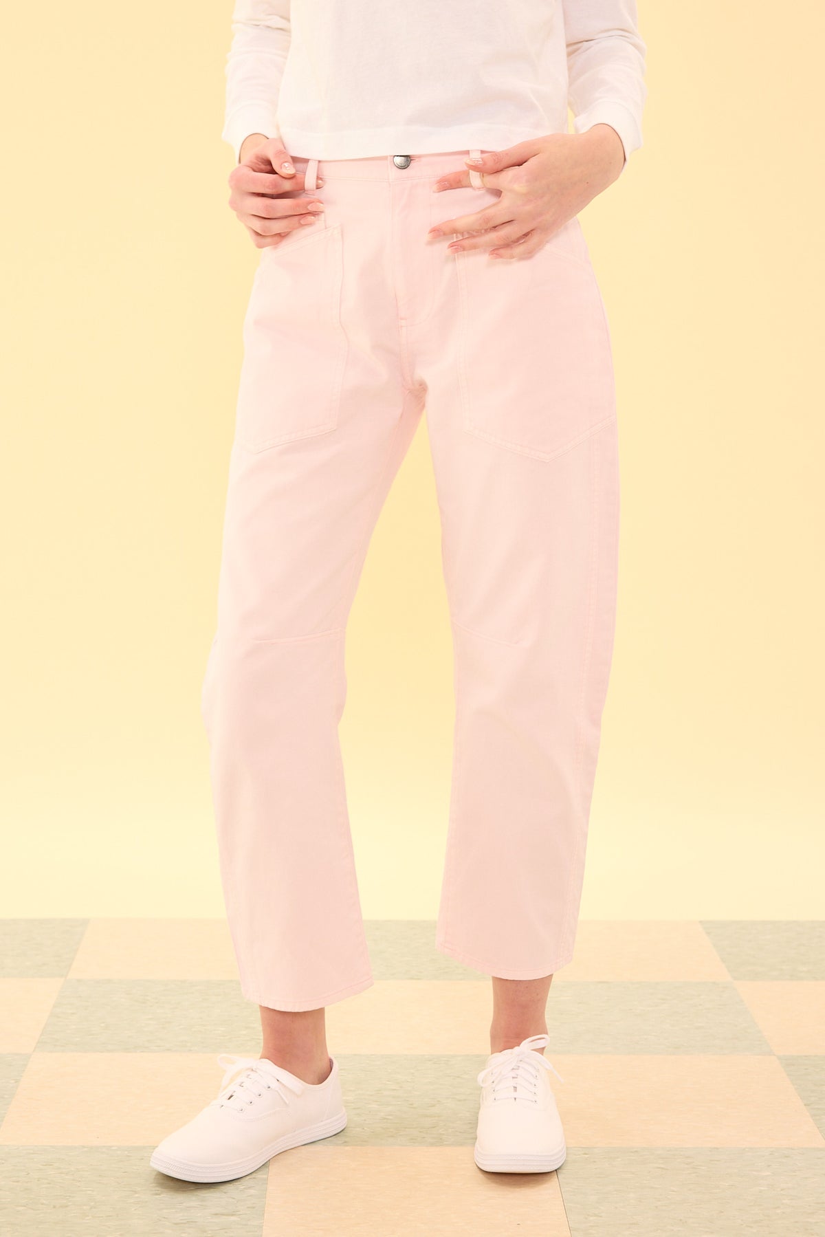 Person wearing light pink pants and white shoes on a pastel yellow background