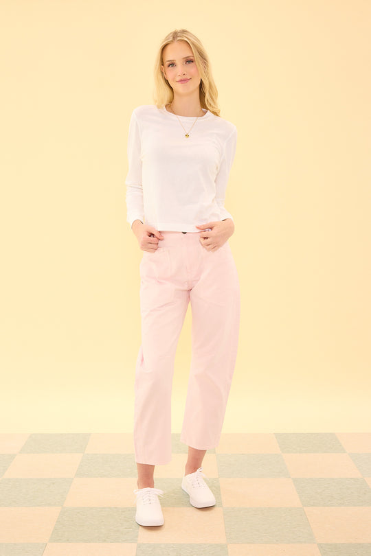Woman wearing a white top and pink pants standing on a checkered floor with a yellow wall background