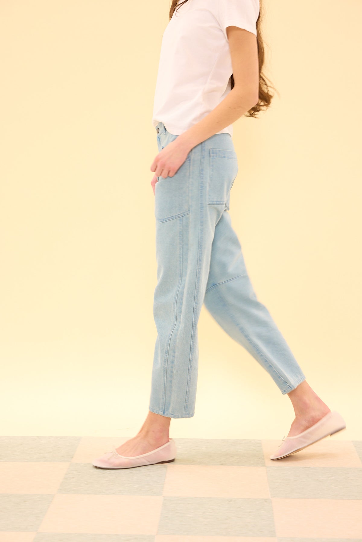 Person wearing light blue jeans and a white shirt on a checkered floor with a yellow wall background