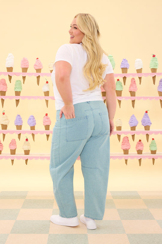 Woman wearing light blue jeans and a white t-shirt in front of an ice cream cone wall.
