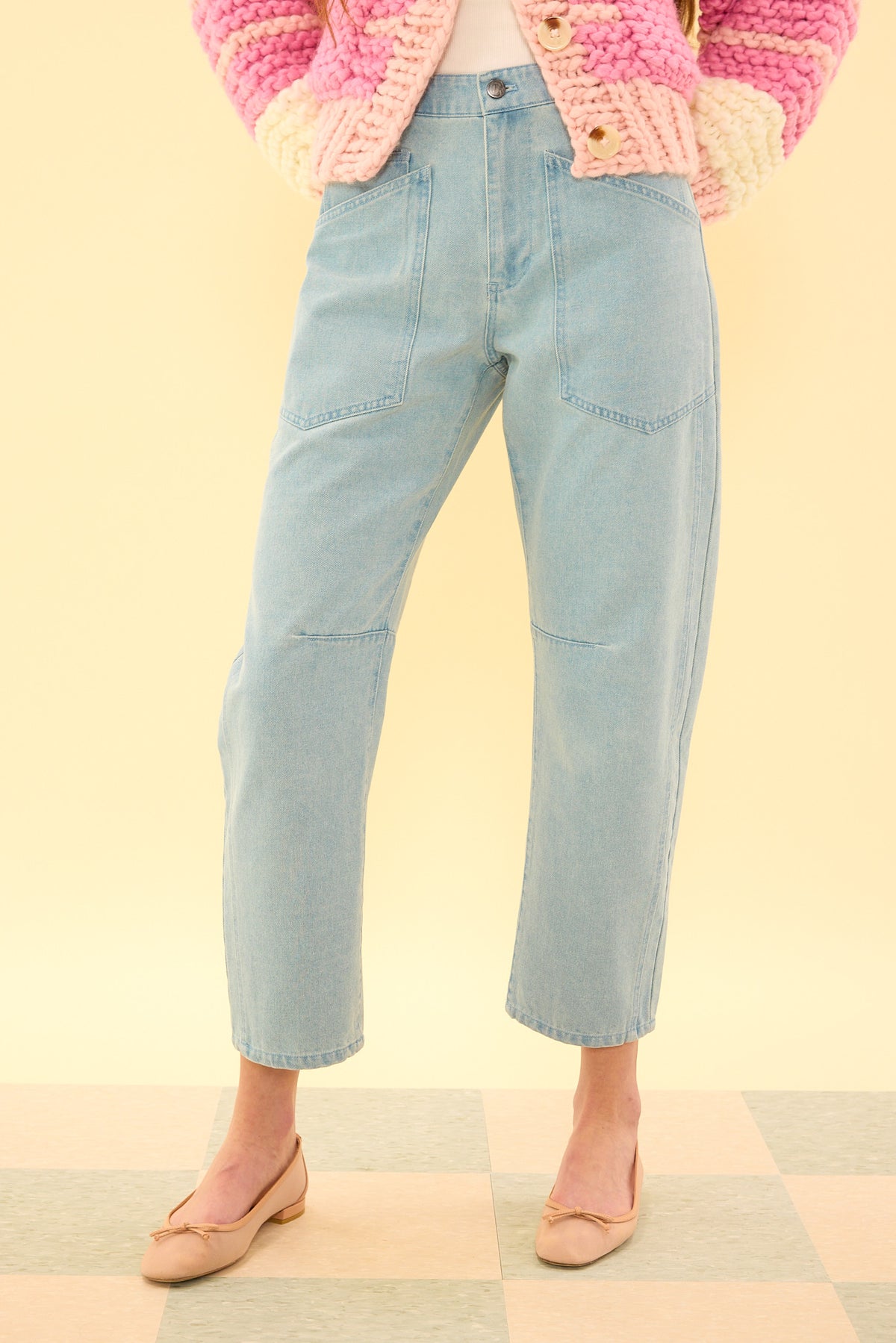 Light blue jeans worn with a pink and white patterned cardigan on a yellow background