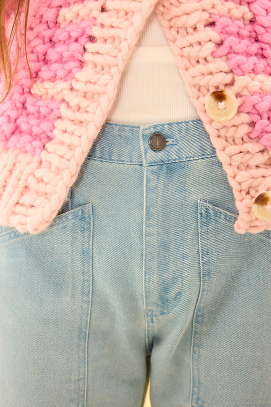 Close-up of a pink knitted cardigan over a white shirt and blue jeans.