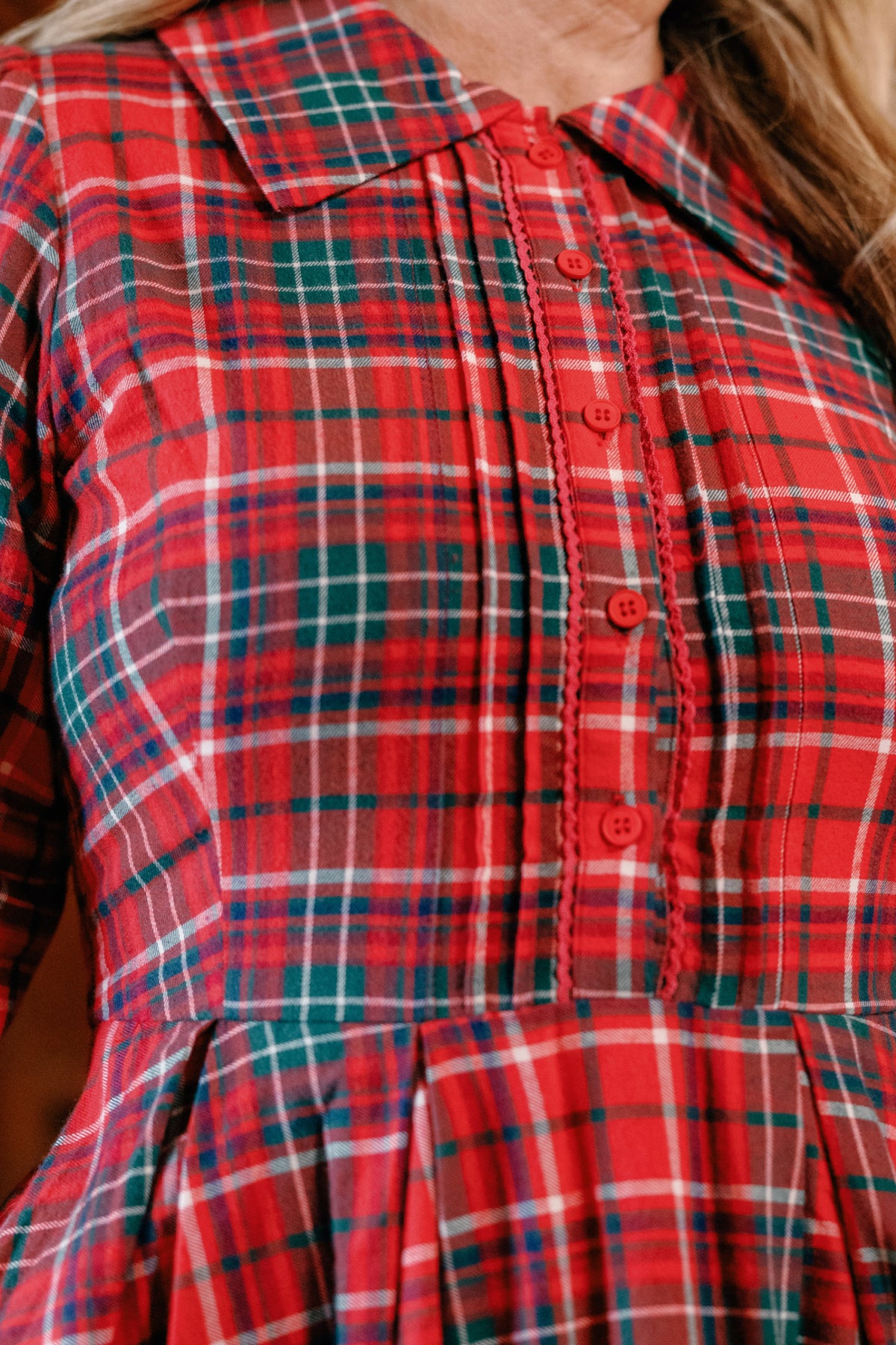 A close-up of a person wearing the Ivy City Co Amber 3/4 Sleeve Dress in Christmas Cheer Plaid, featuring a collared neckline, button-down front, and festive intersecting lines in red, green, white, and navy blue—making it the perfect girls Christmas dress.