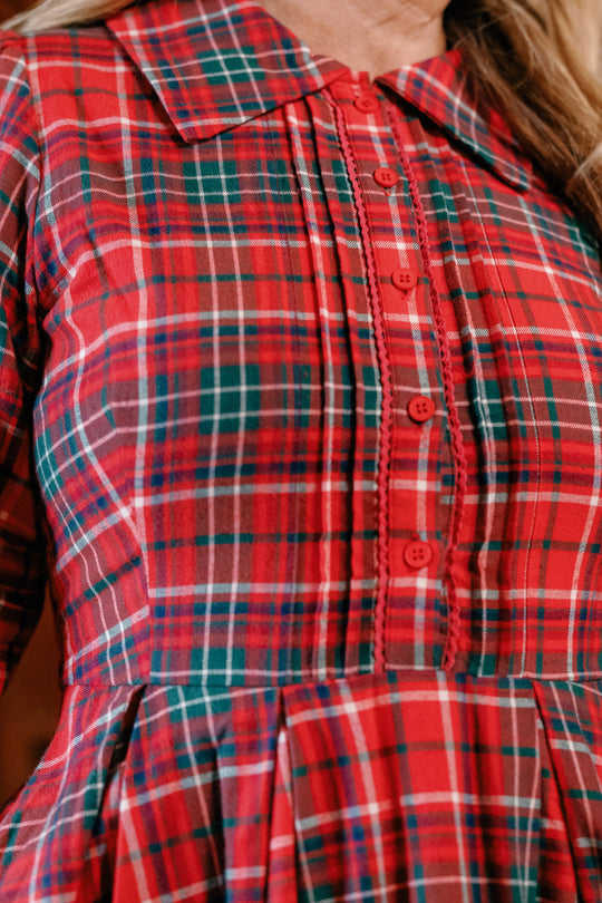 A close-up of a person wearing the Ivy City Co Amber 3/4 Sleeve Dress in Christmas Cheer Plaid, featuring a collared neckline, button-down front, and festive intersecting lines in red, green, white, and navy blue—making it the perfect girls Christmas dress.