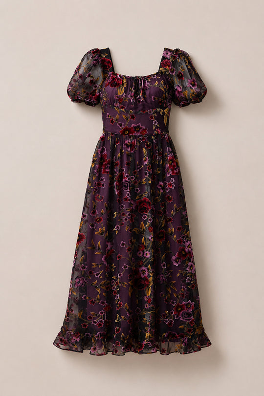 Introducing the Amira Dress in Violet Dusk Burnout by Ivy City Co—a purple, ankle-length maxi dress crafted from sheer fabric and adorned with red, pink, and yellow floral patterns. Featuring puffed short sleeves, a square neckline, pockets for added functionality, and a ruffled hem, this elegant dress effortlessly blends style and practicality.