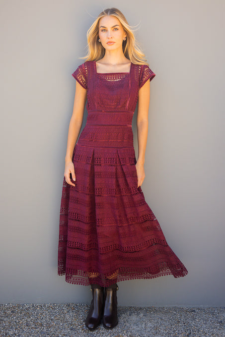 Woman wearing a burgundy lace dress against a plain background