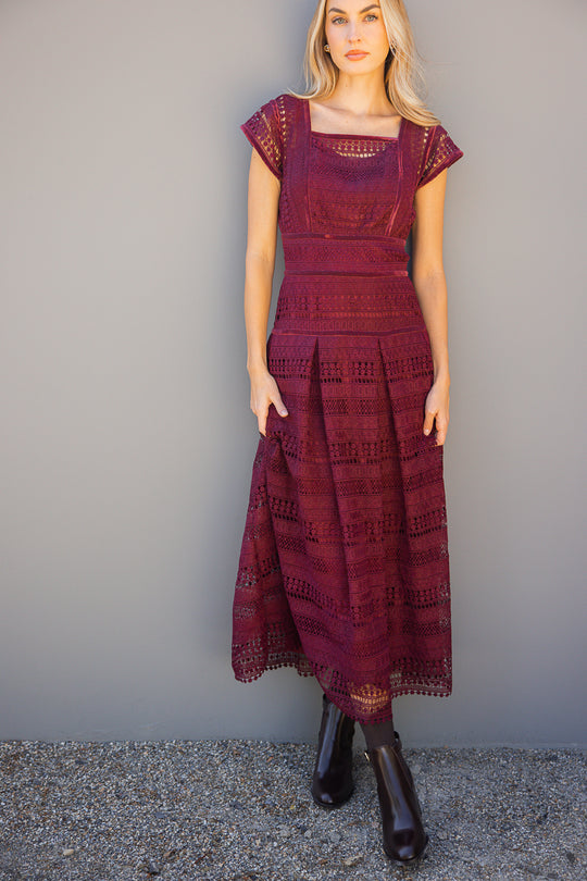 Woman wearing a burgundy lace dress against a gray background