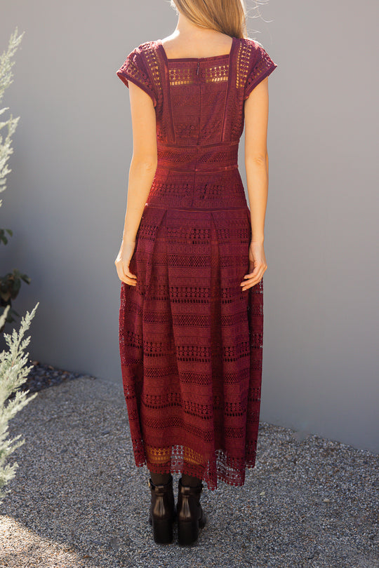 Woman wearing a burgundy patterned dress standing against a gray wall.