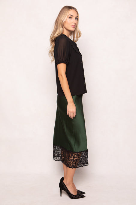 Woman wearing a black top and green skirt with lace hem on a white background