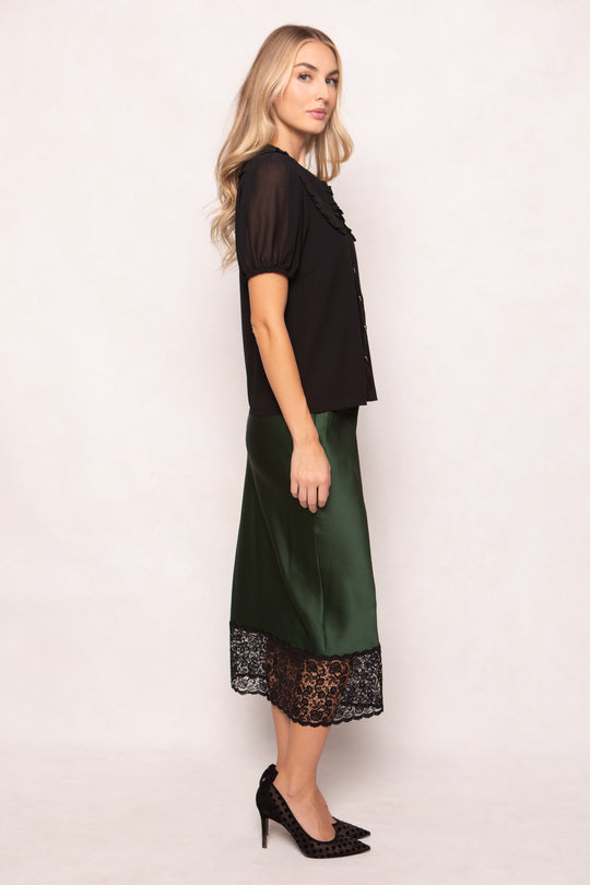 Woman wearing a black top and green skirt with lace hem on a white background
