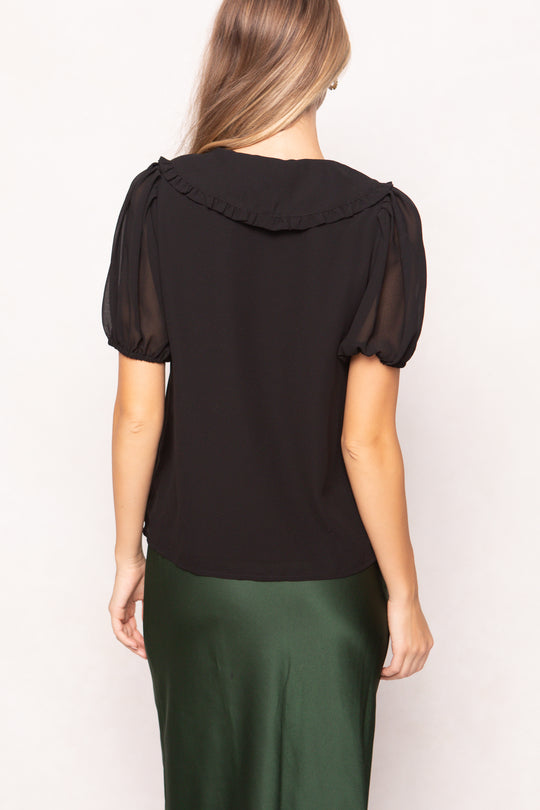 Woman wearing a black blouse with sheer sleeves on a white background
