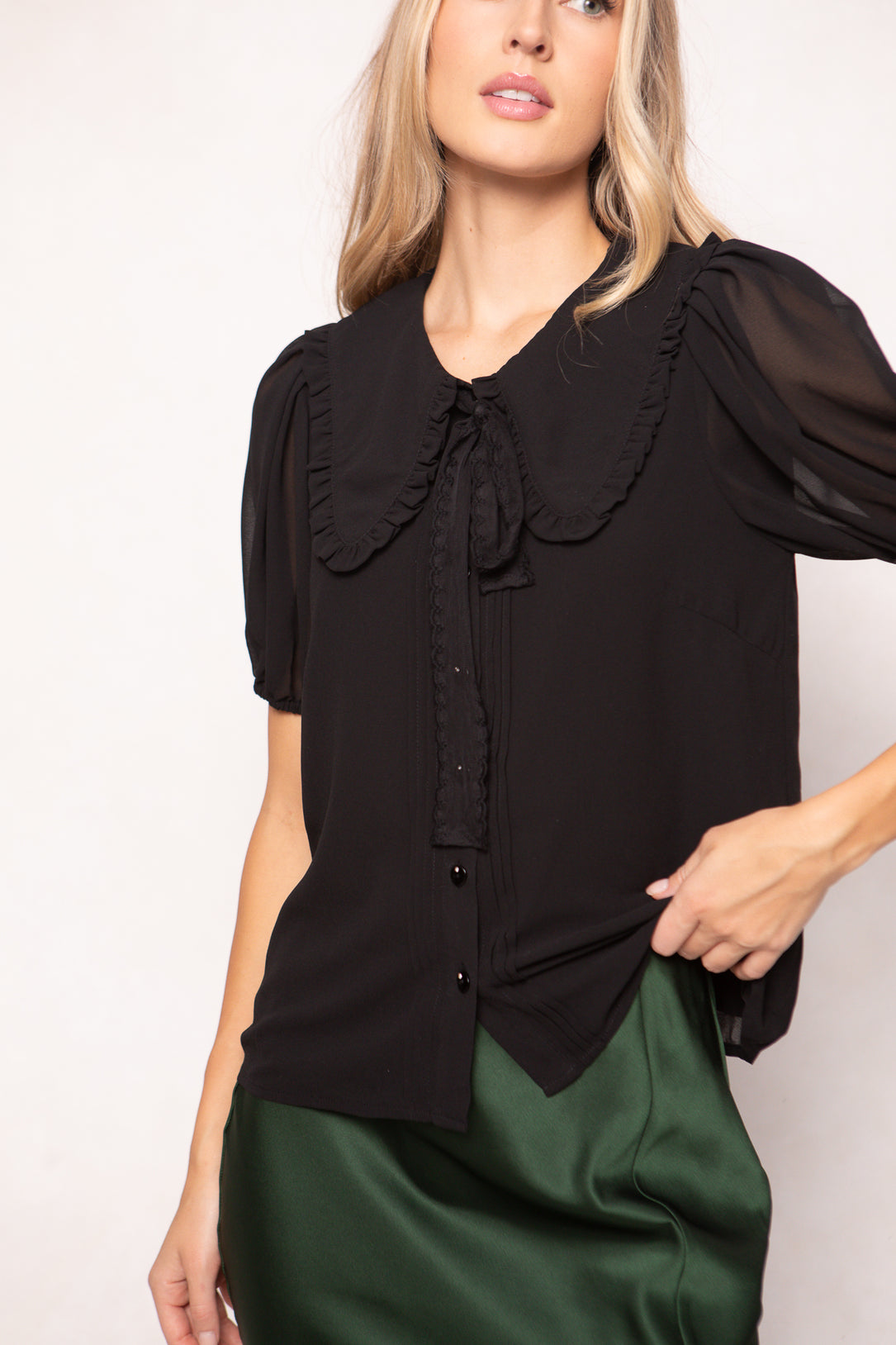 Woman wearing a black blouse with a ruffled collar against a white background